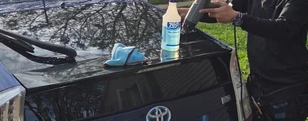 Close view of an installer's hands, a heat tool and film on the glass of a blue Toyota Prius.